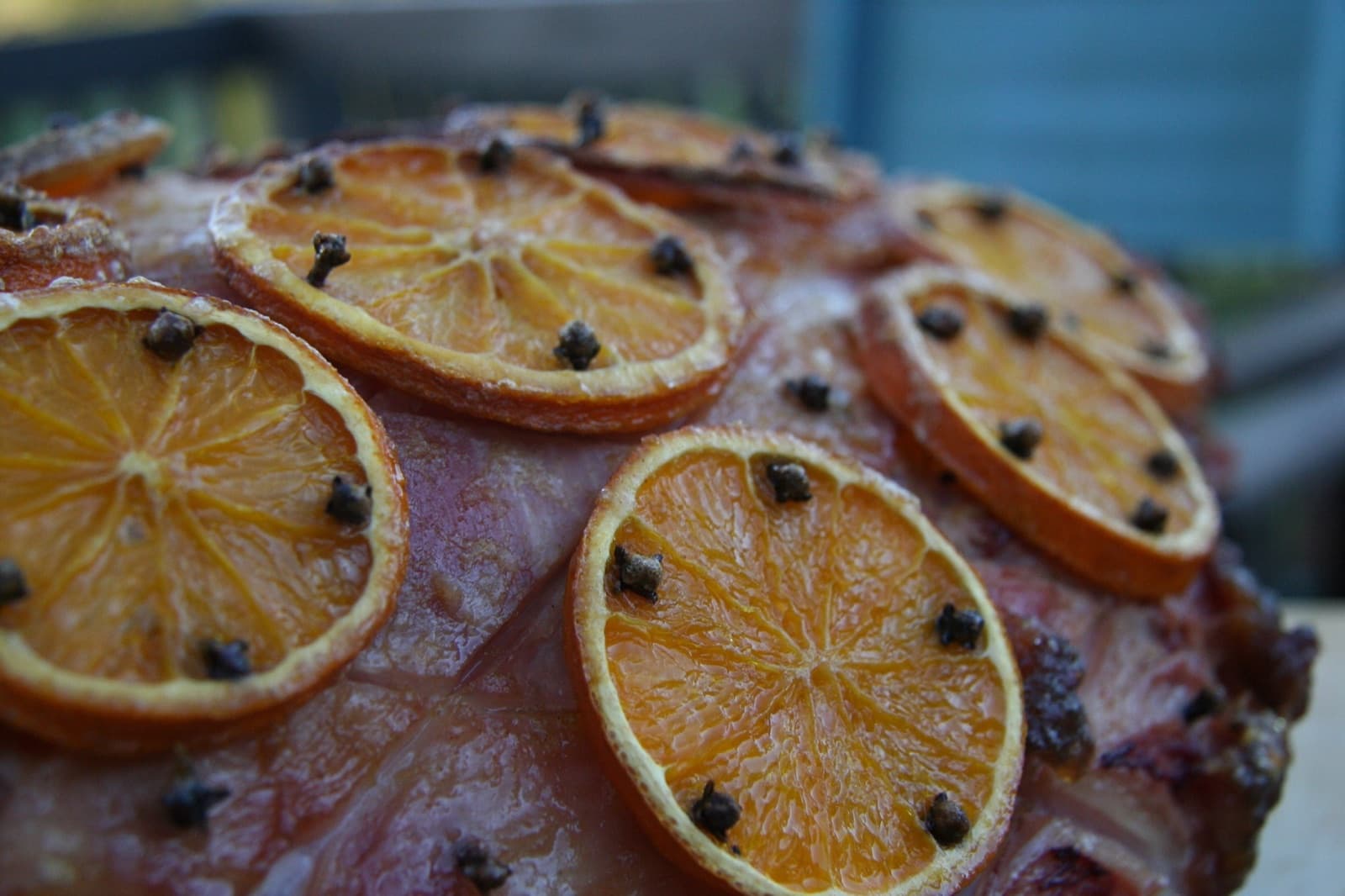 A close-up of a glazed ham studded with cloves and topped with caramelized orange slices.