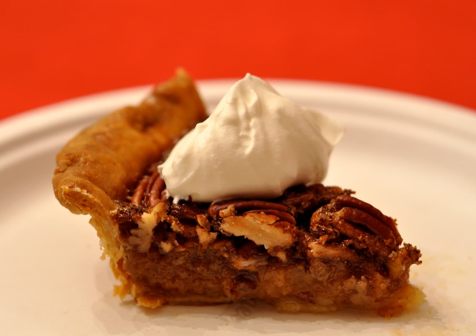 A slice of pecan pie on a white plate, topped with a spoonful of whipped cream.